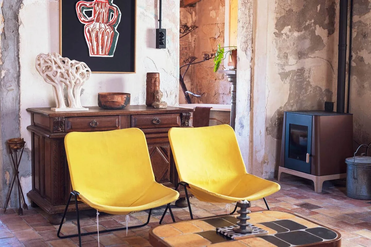 Samena : un salon aux murs de pierre, deux fauteuils jaunes et un poêle.