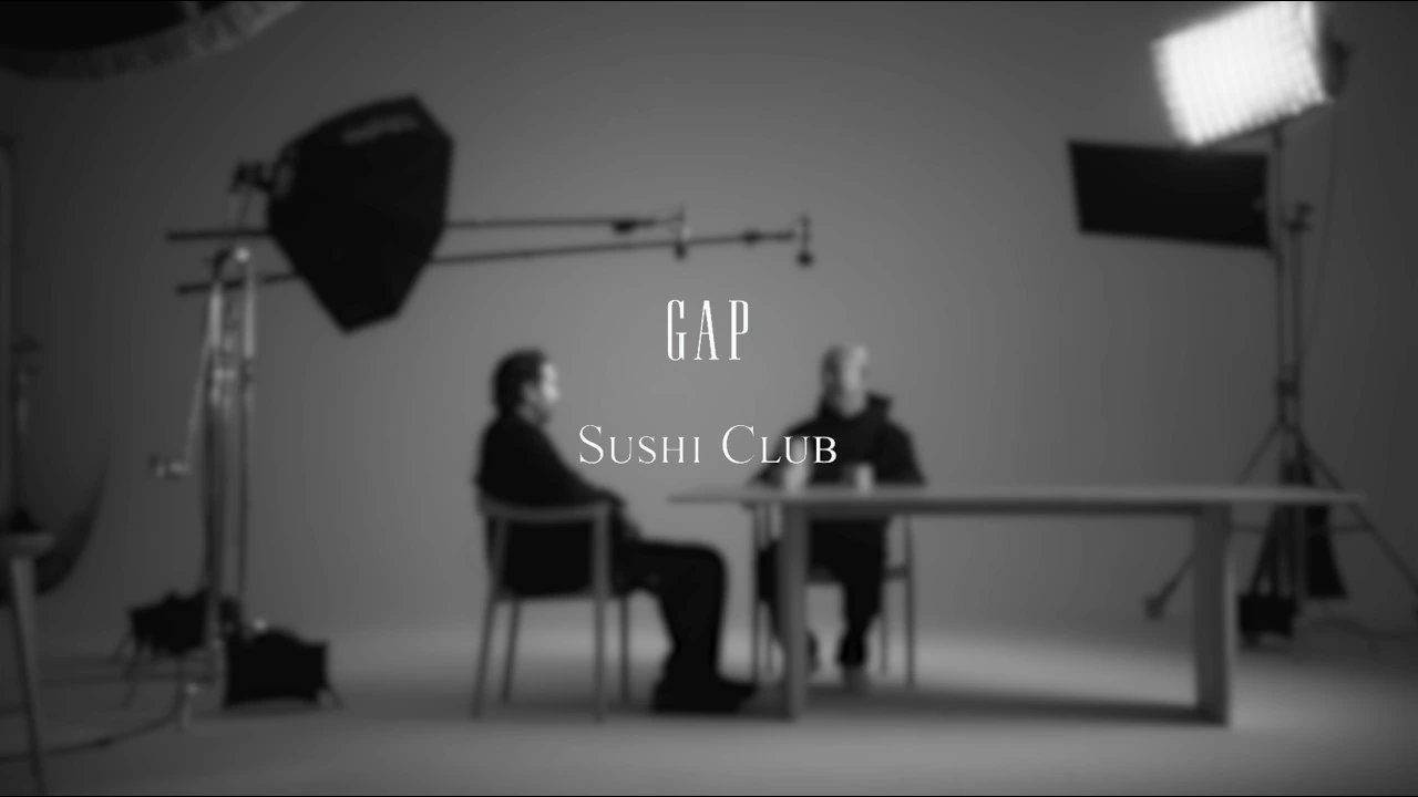 Image officielle du film Gap × Sushi Club : deux personnes assises face à face sur un plateau nu, projecteurs visibles.